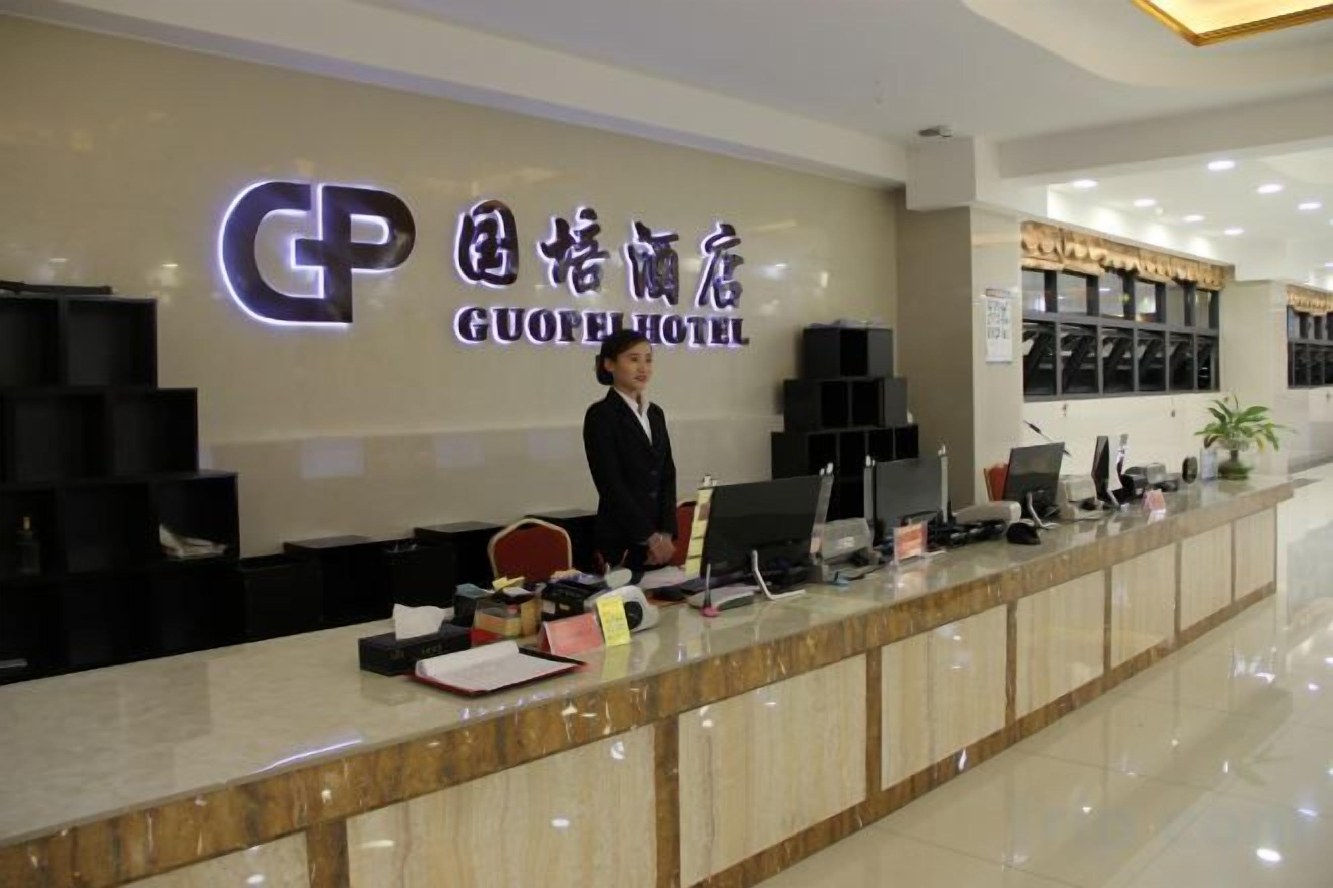 A hotel reception desk with a sign indicating the hotel name, a receptionist, and a counter with various items.