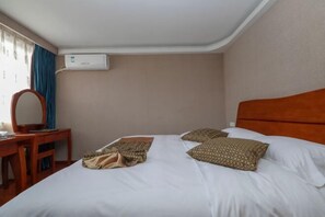 Habitación de hotel con una cama, un escritorio de madera, una silla, un espejo y un equipo de aire acondicionado en la pared.