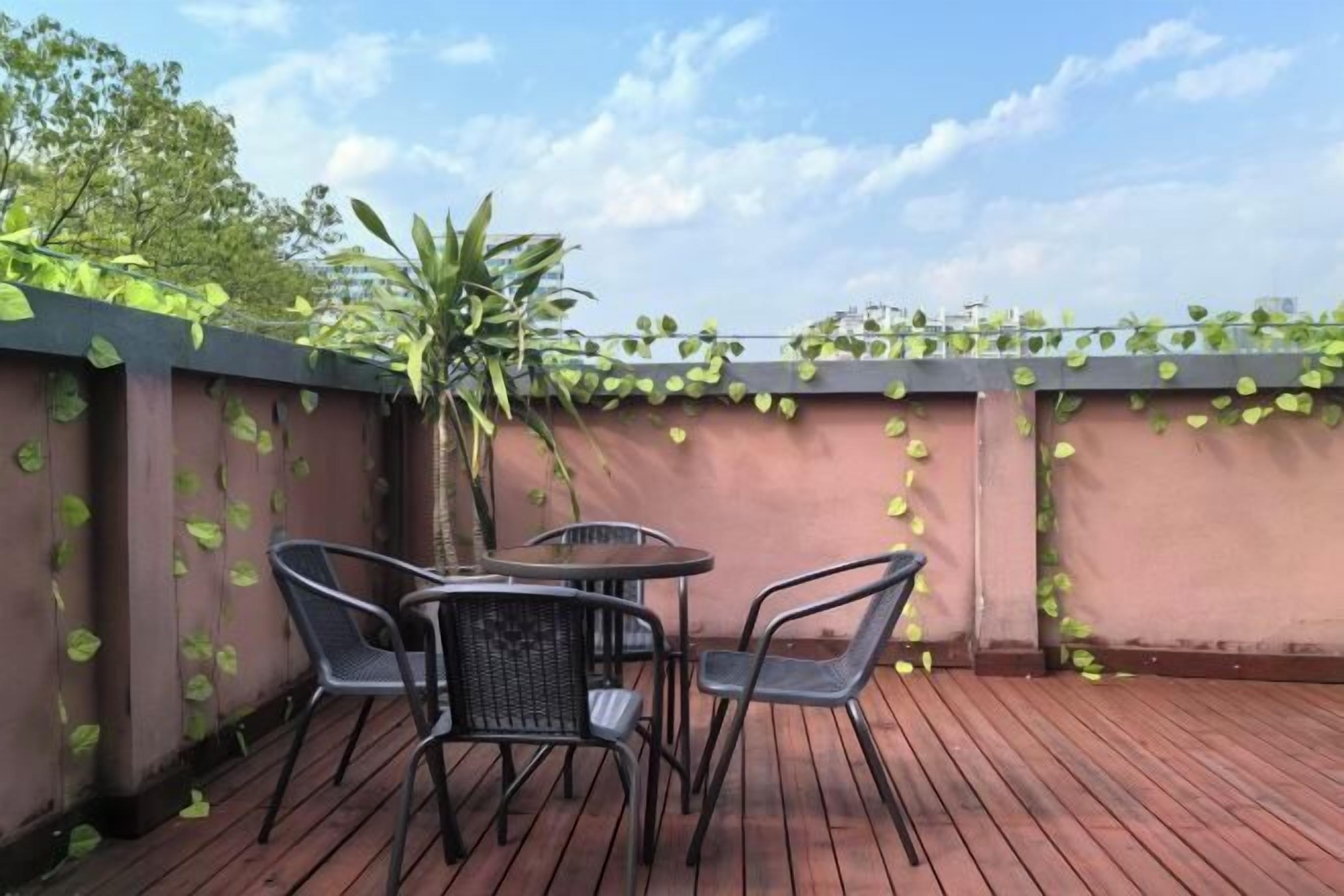 Un patio al aire libre con una mesa y sillas, rodeado por una terraza de madera y una pared cubierta de enredaderas verdes.