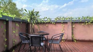 Un patio al aire libre con una mesa y sillas, rodeado por una terraza de madera y una pared cubierta de enredaderas verdes.