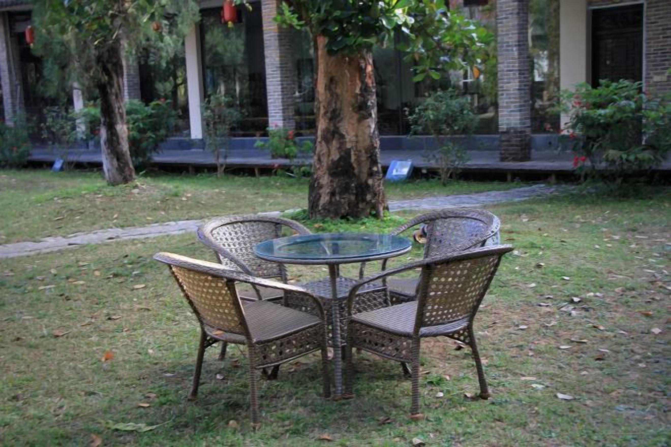 A round glass table with wicker chairs in a grassy outdoor area.