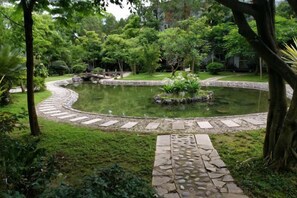 A circular pond with a stone pathway leading to it, surrounded by lush greenery. - Pu'er Guopei Hotel (Pu'er)
