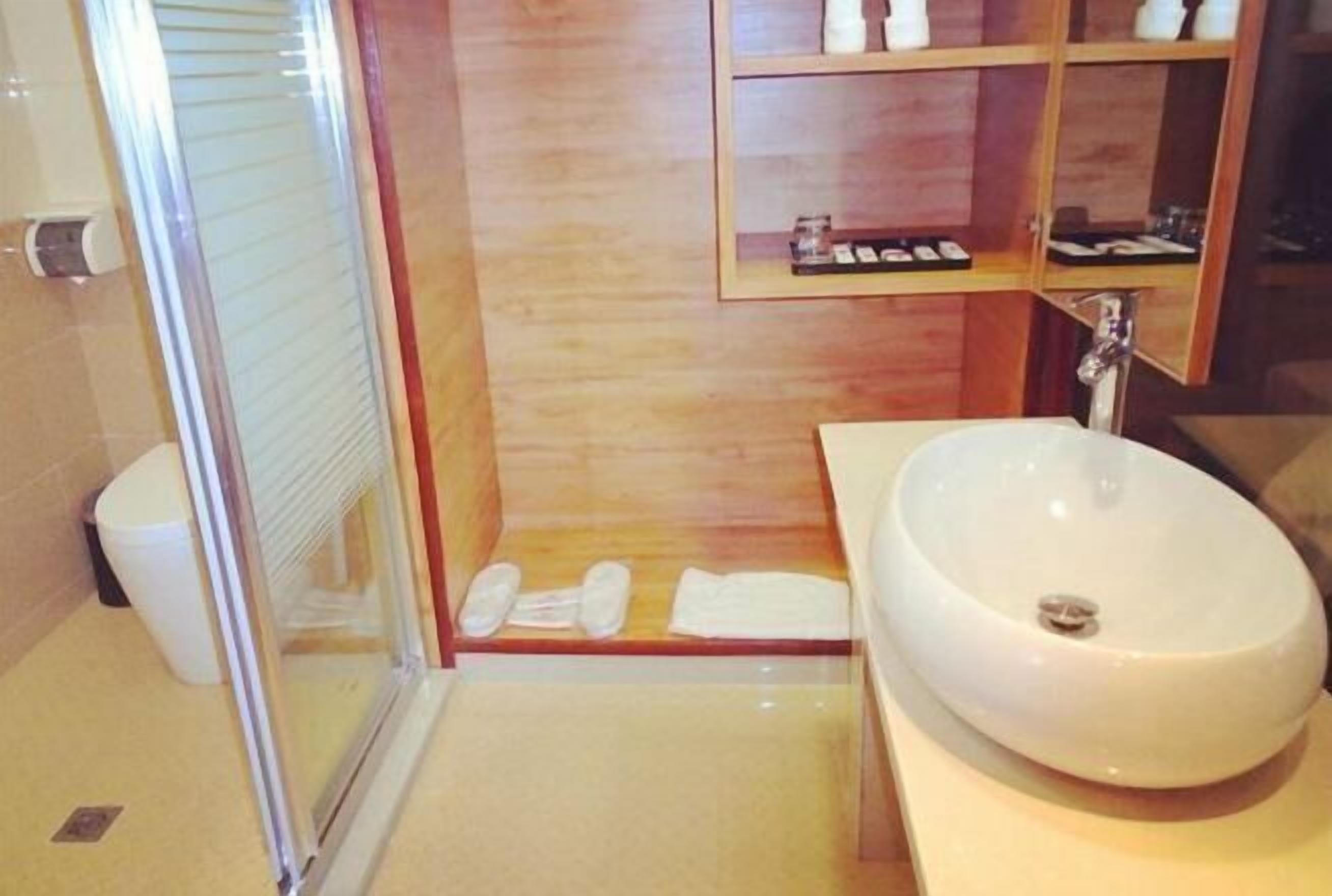 Ein modernes Badezimmer mit Duschkabine aus Glas, einem weißen Waschbecken und einem Holzkosmetikschrank mit Spiegel.