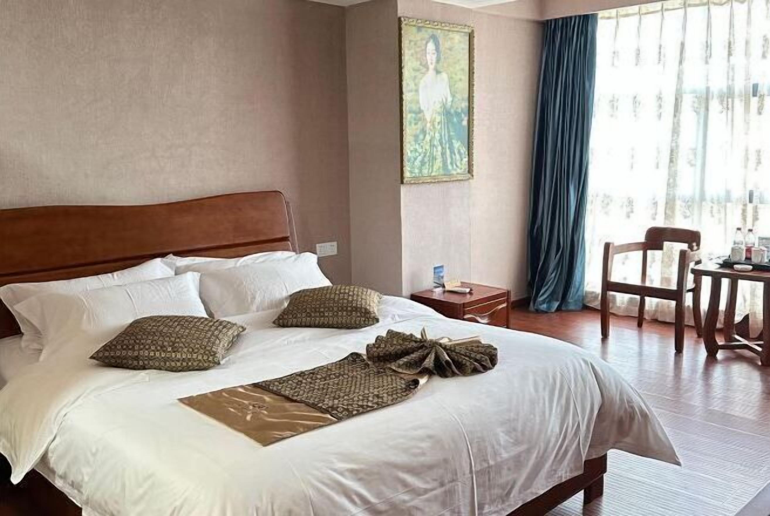 Une chambre d’hôtel avec un grand lit, une tête de lit en bois, une table de chevet, une chaise et une fenêtre avec des rideaux.