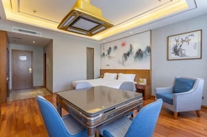 Habitación de hotel con cama, escritorio y sillas. Hay un cuadro en la pared y una puerta que da a otra habitación.