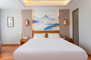 Une chambre d’hôtel avec un grand lit, deux tables de chevet, une commode, un tableau au mur et deux lampes fixées au mur.