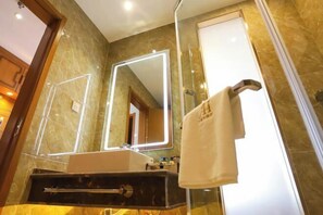 Un baño con lavamanos de mármol, un espejo grande con luces LED y una toalla colgada en un perchero.