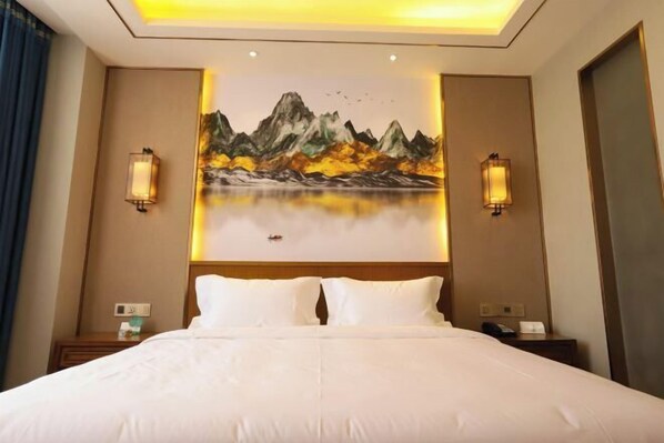 A hotel room with a large bed, two bedside tables, a painting of mountains, and wall sconces.
