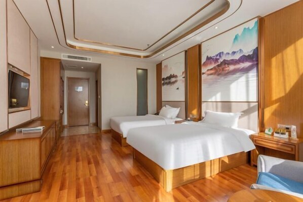 Une chambre d’hôtel avec deux lits, un plancher en bois, une télévision, un tableau et un bureau avec une chaise.