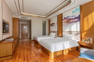 Habitación de hotel con dos camas, suelo de madera, televisión, un cuadro y un escritorio con silla.