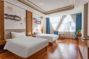 Habitación de hotel con dos camas, suelo de madera, un escritorio, una silla y obras de arte en las paredes.