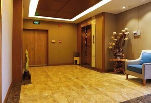 A hotel lobby with a marble floor, wooden doors, a reception desk, and a blue chair.