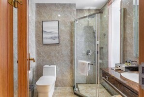 A modern bathroom with a glass shower enclosure, a marble-tiled wall, a white toilet, and a wooden vanity with a mirror.