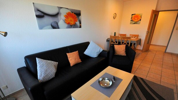 A living room with a black sofa, a wooden coffee table, and a dining area with wooden chairs and a table.