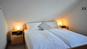 A single bed with white linens in a room with sloped ceilings. There are two bedside tables with lamps, one on each side of the bed.