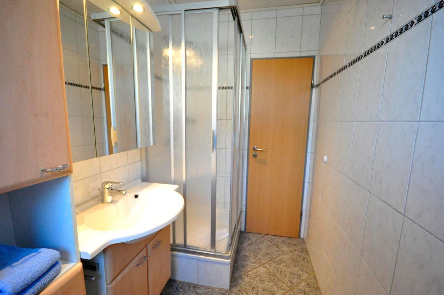 Ein Badezimmer mit Waschbecken, Spiegel, Duschkabine und Holztür.