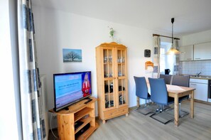 A modern living room with a television, wooden cabinet, dining table, and chairs.