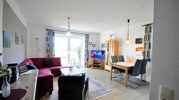 Ein Wohnzimmer mit rotem Sofa, Couchtisch, Fernseher und einem Essbereich mit Stühlen und Tisch.