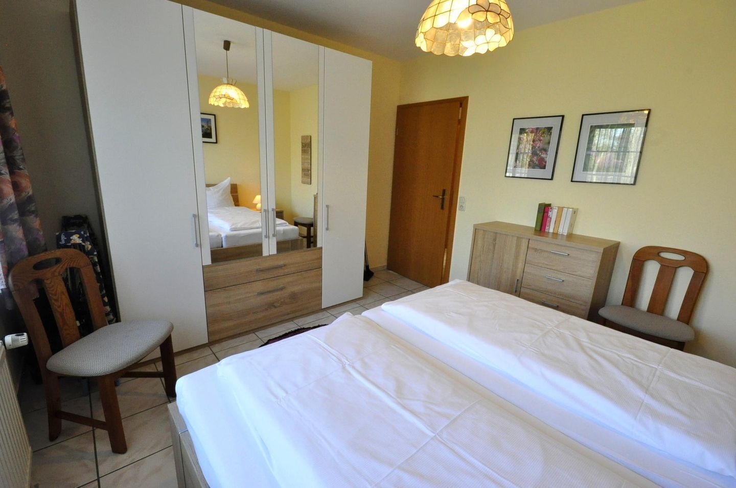 Ein Schlafzimmer mit Bett, Kleiderschrank, Stuhl, Kommode und einer Tür.