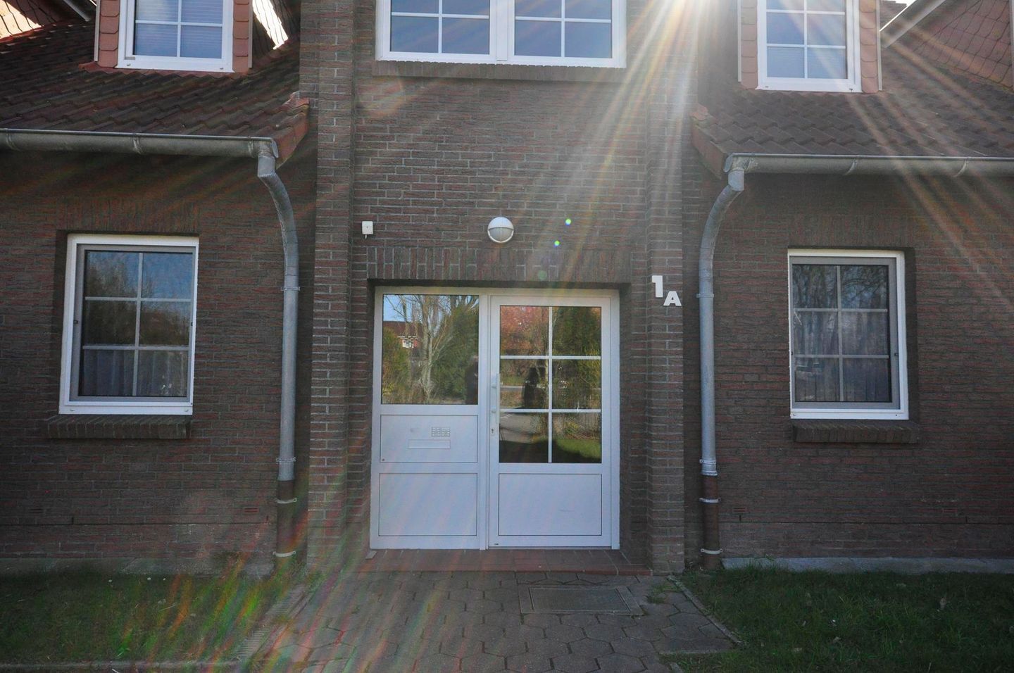 Een tweelaags bakstenen gebouw met een centrale ingang, twee ramen aan elke kant, en het cijfer '1A' zichtbaar aan de rechterkant.