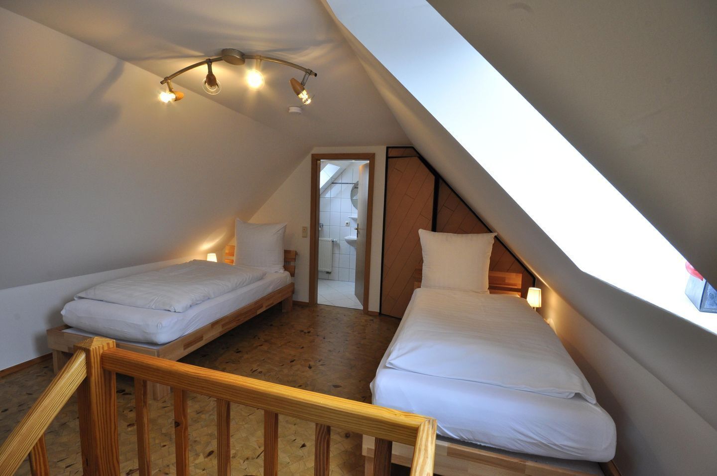 A small, attic-style bedroom with two single beds, wooden flooring, and a sloped ceiling with skylights.