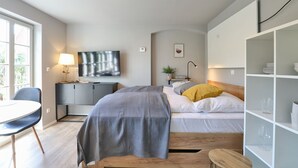 Camera da letto moderna con un letto, comodino, televisione e una piccola area studio.