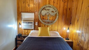 Un dormitorio con pared de madera, una cama con colcha estampada, una almohada amarilla y dos lámparas de noche.