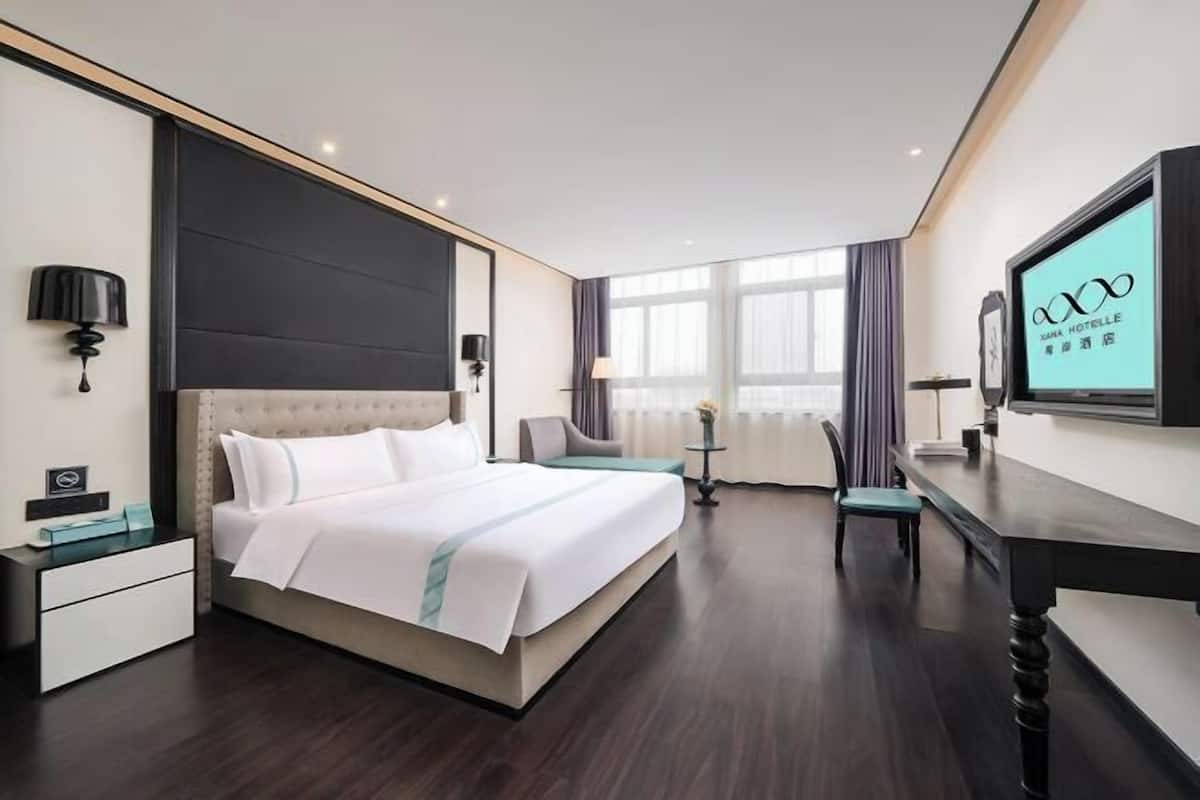 Habitación de hotel con cama, mesita de noche, lámpara, televisor y vistas al exterior.