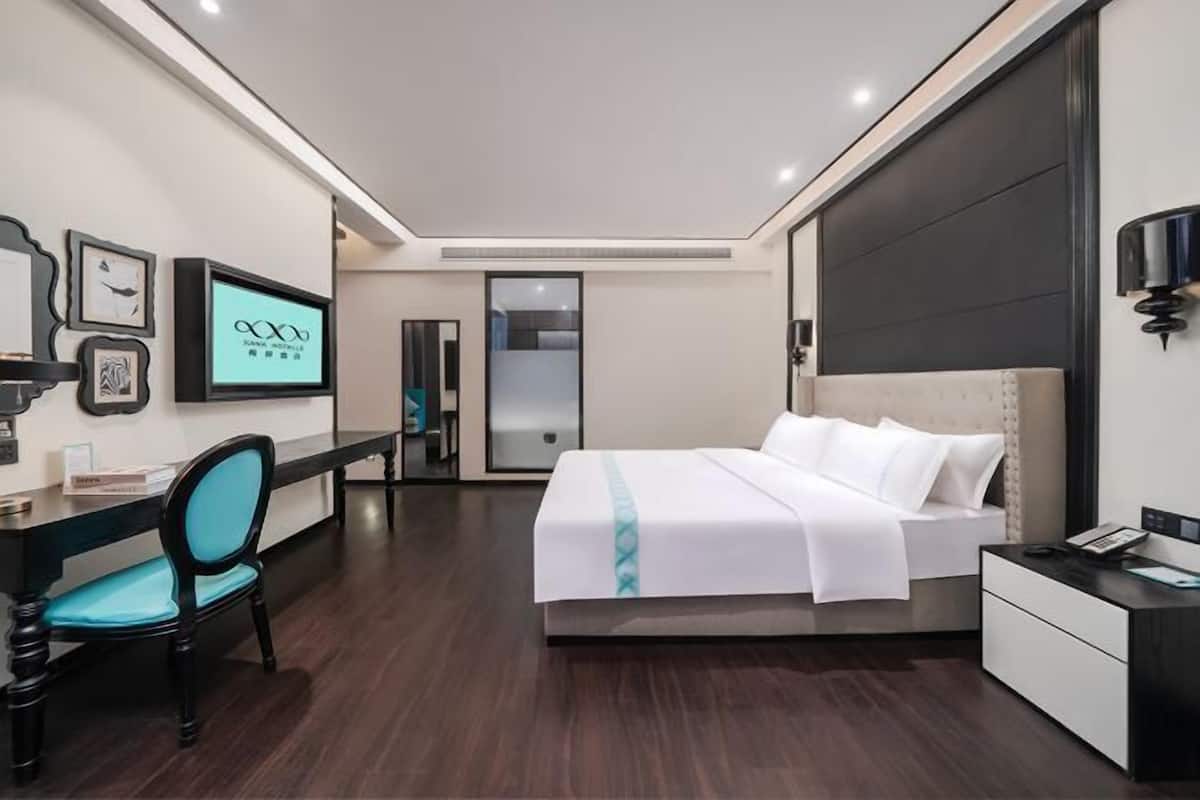 Una habitación de hotel moderna con cama, escritorio, silla y televisor en la pared.