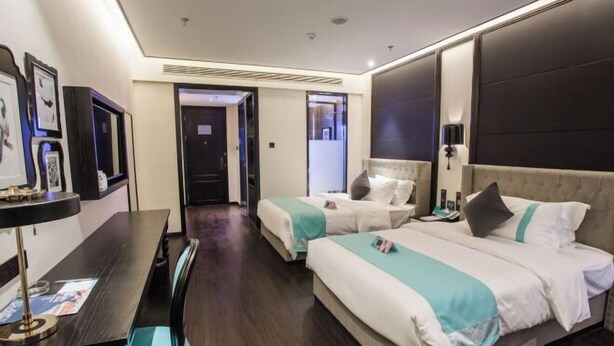 Habitación de hotel con dos camas, un escritorio y una silla. Se ve una puerta que da a otra habitación y una pared con cuadros enmarcados.