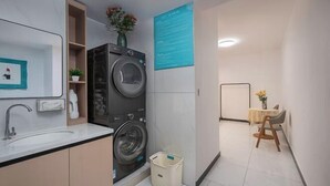 Un baño moderno y funcional, con lavadora incorporada, un lavamanos y una pequeña mesa con una silla.