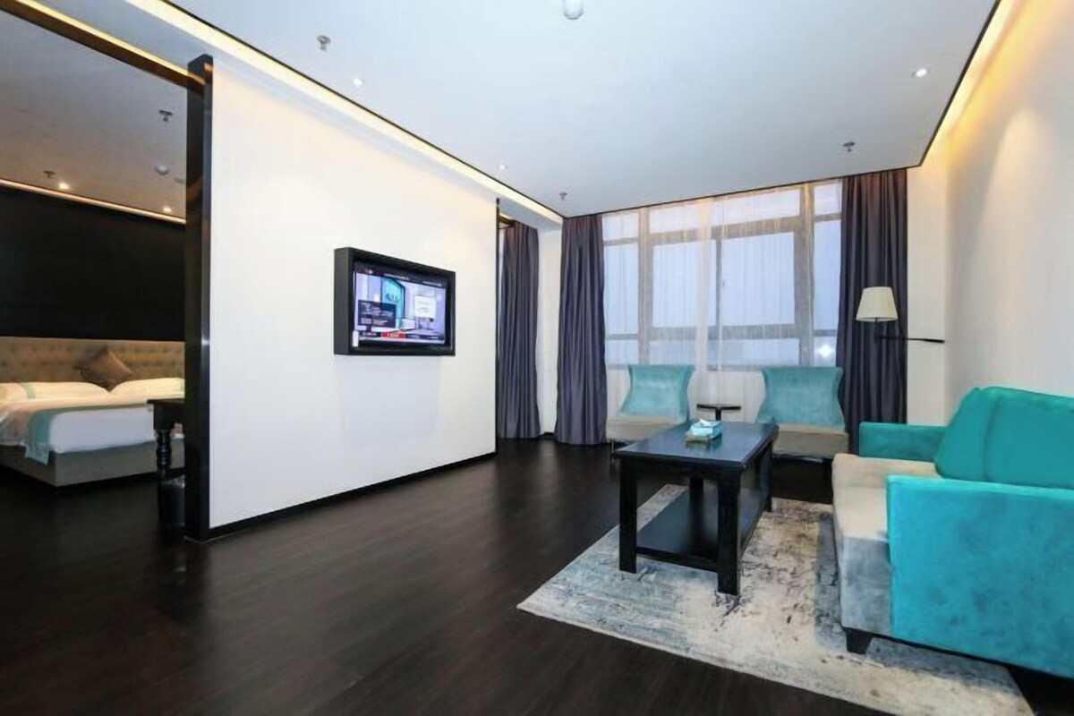 A modern hotel room with a bed, a sofa, a TV, and a large window.