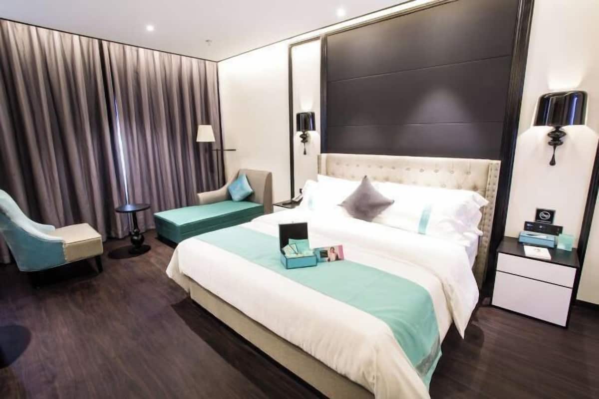 Una habitación de hotel moderna con una cama grande, un sofá independiente, una mesita pequeña y una mesita de noche.