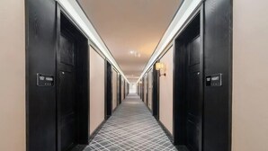 Un pasillo de hotel con puertas negras, placas de habitaciones numeradas y un suelo estampado.