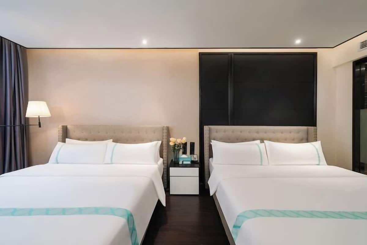 Habitación de hotel con dos camas, una mesita de noche, una lámpara y un ventanal grande.