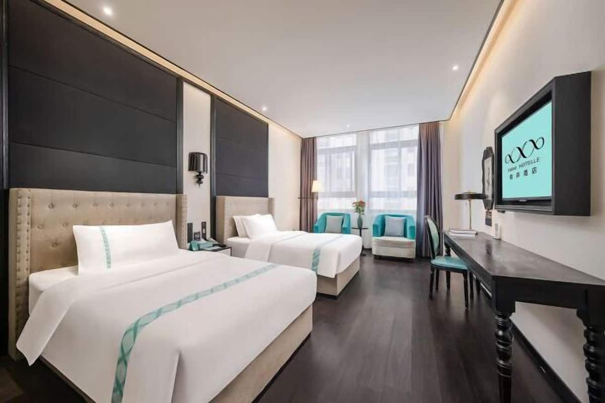 Una habitación de hotel con dos camas, un escritorio, un televisor y una ventana con cortinas.