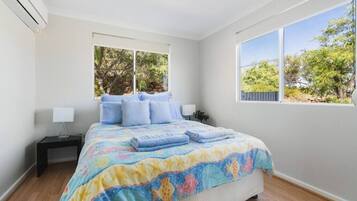 A bedroom with a bed, two windows, a nightstand, and a wall-mounted air conditioner.