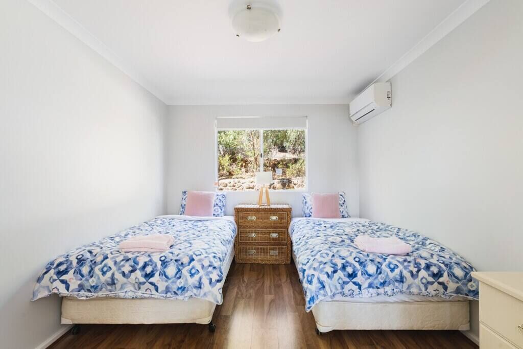 A bedroom with two beds, a window with a view of greenery, a ceiling light, and a wall-mounted air conditioner.