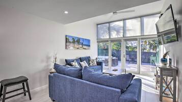 A modern living room with a blue sofa, a small stool, and a painting of a beach scene.