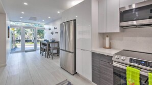 A modern kitchen with stainless steel appliances, a dining area with a table and chairs, and a view through glass doors to the outside. - Canal-Front Condo: Walk to Downtown Ft Lauderdale! (Fort Lauderdale)