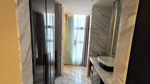 Ein modernes Badezimmer mit Marmorboden, einem großen Spiegel und einem gebogenen Waschbecken.