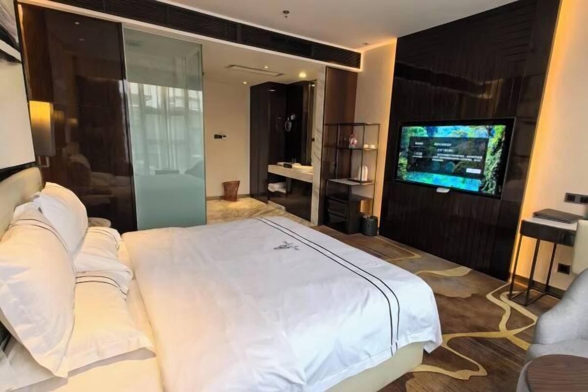 Moderni hotellihuone, jossa on suuri sänky, televisio ja liukuovi, joka johtaa kylpyhuoneeseen.