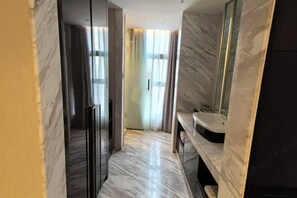 A hallway with a marble floor, a dark door, and a bathroom with a sink and mirror.