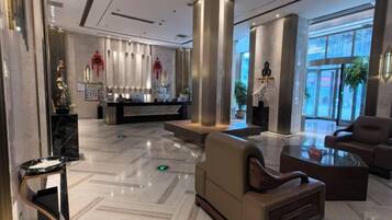 A hotel lobby with a reception desk, seating area, and large windows.