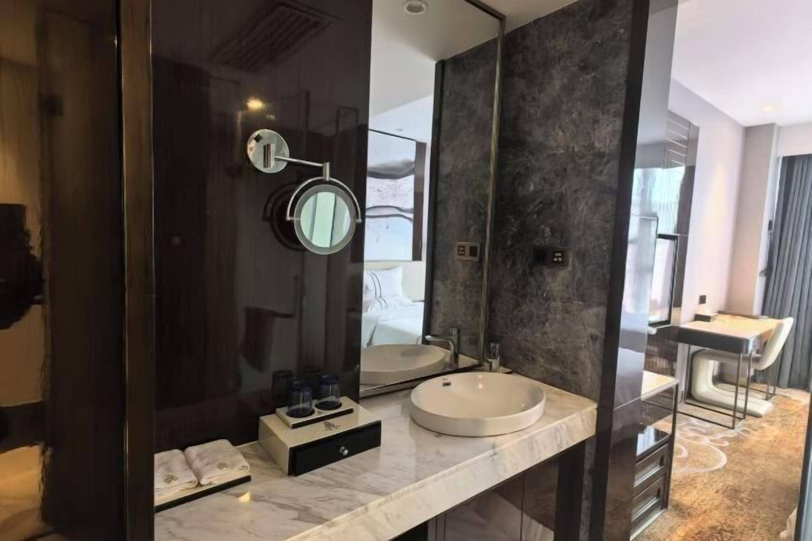 A modern bathroom with a large mirror, a round sink, and a dark marble wall.