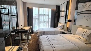 Ein Hotelzimmer mit zwei Betten, einem Schreibtisch und einem großen Fenster mit Vorhängen.