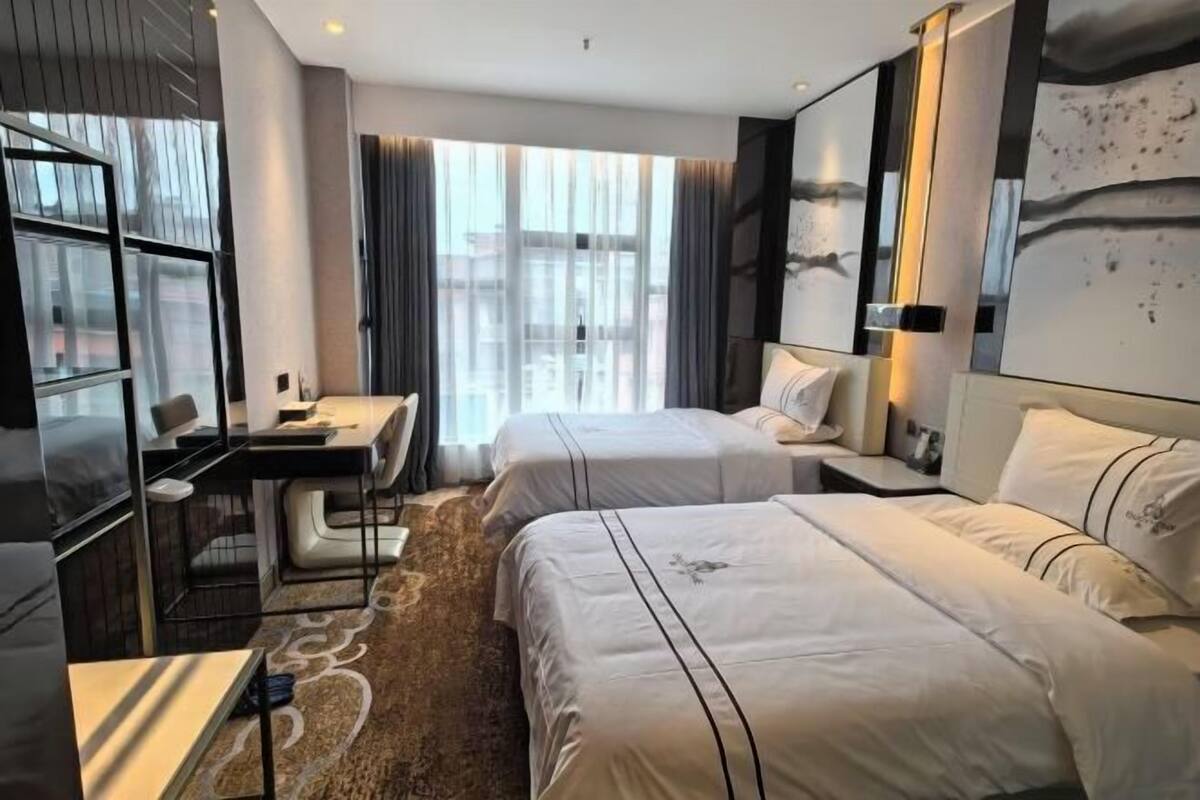 Hotellihuone, jossa on kaksi sänkyä, työpöytä ja suuri ikkuna, jossa on verhot.