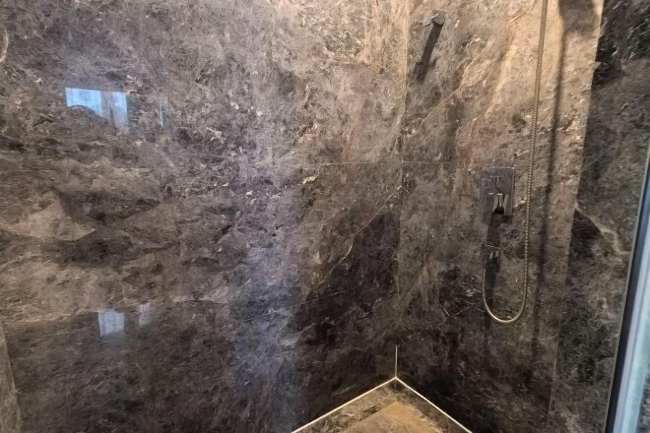 A bathroom with a dark marble wall, a shower area, and a glass door.
