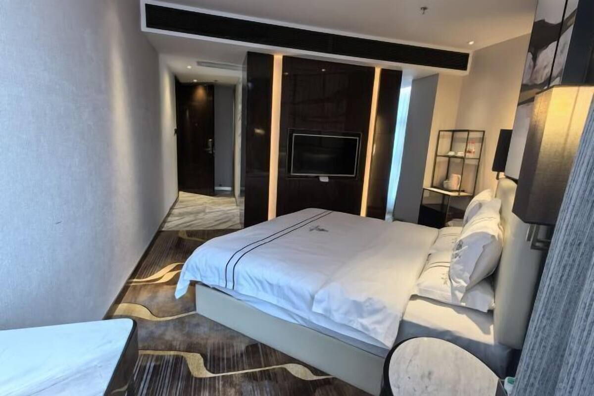 Moderni hotellihuone, jossa on suuri sänky, seinälle asennettu televisio, yöpöytä ja tuoli.