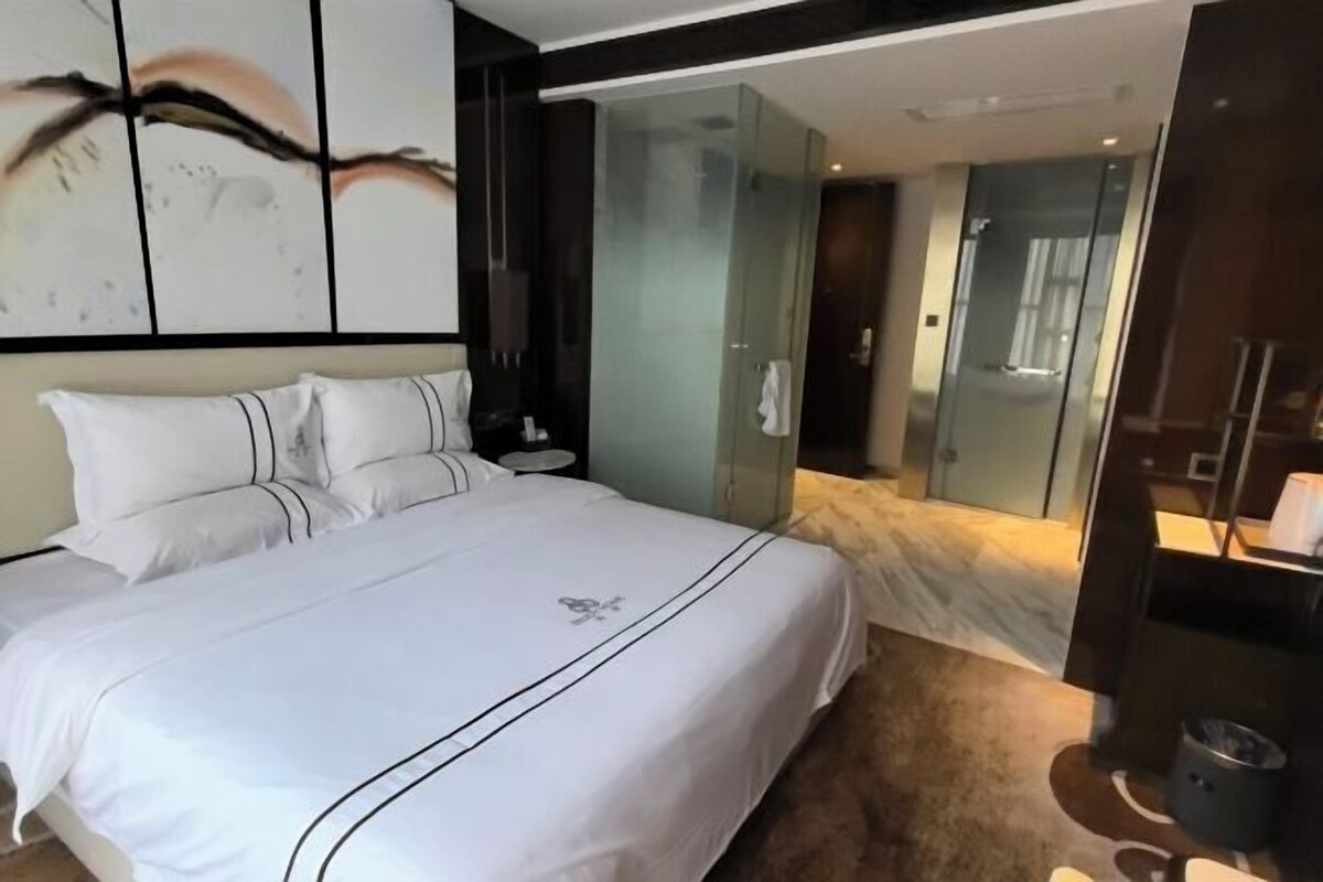 A modern hotel room with a large bed, a glass shower enclosure, and a small bedside table.